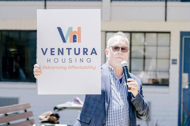 Jeffrey holding a Ventura Housing sign with a microphone