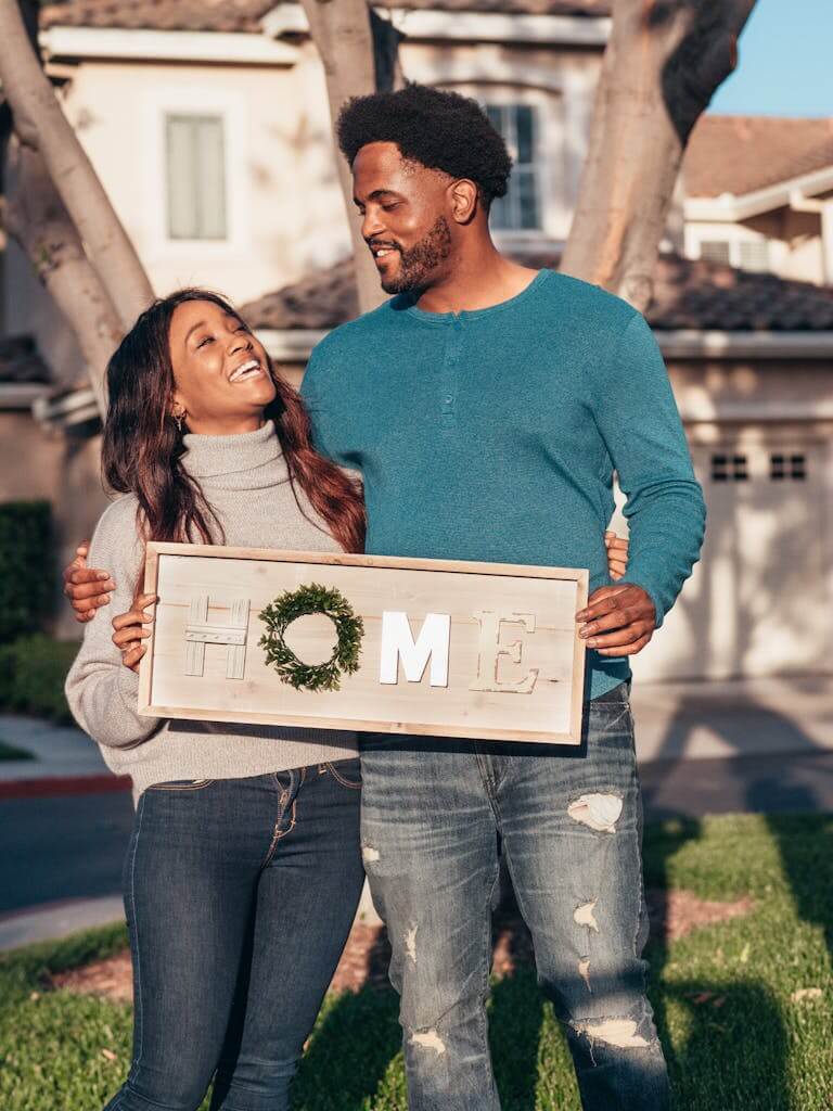 A joyful couple holding a 'home' sign, symbolizing new homeownership.